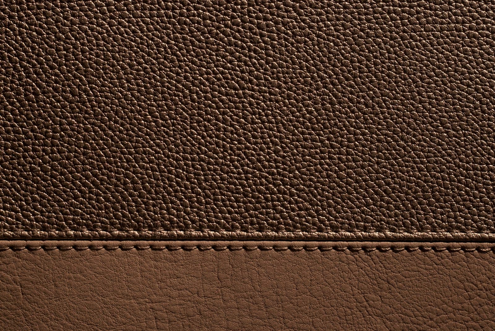 Dense pebbled grain breaking against a smooth panel, divided by a single hand-set saddle stitch